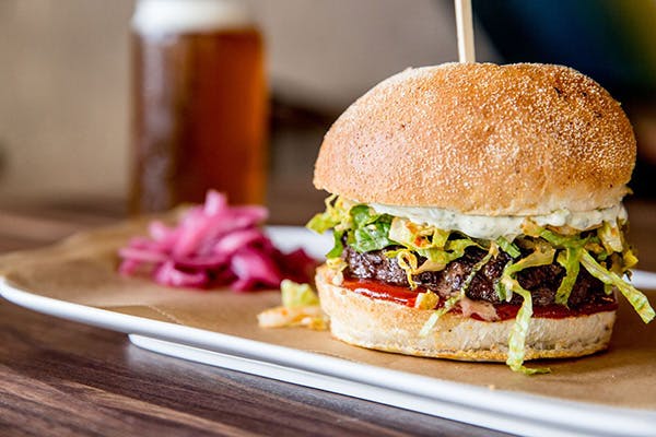 a big burger with shredded lettuce, meat, red sauce and some red onion on the side