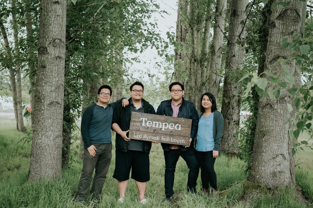 4 people holding a wooden sign that says tempon