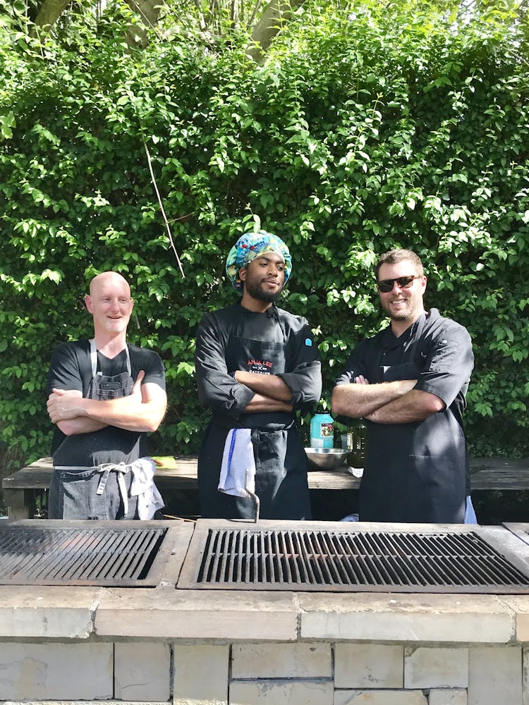 3 men with their arms crossed in front of a grill