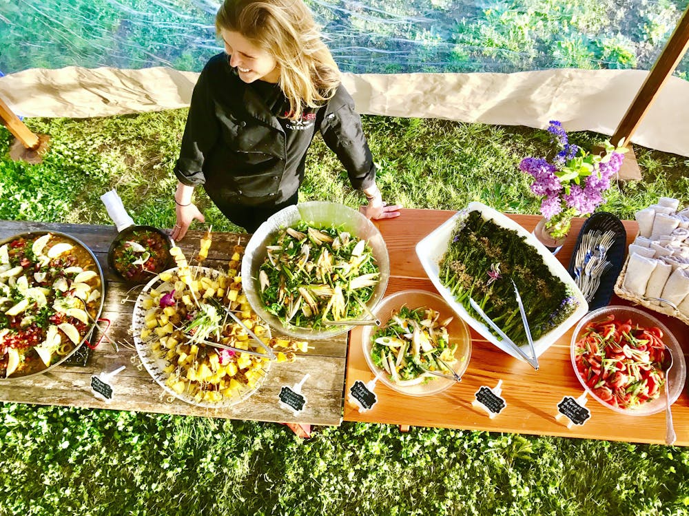 an overhead shot of Chef Anja standing in front of a buffet of food all served on long tables on top of grass