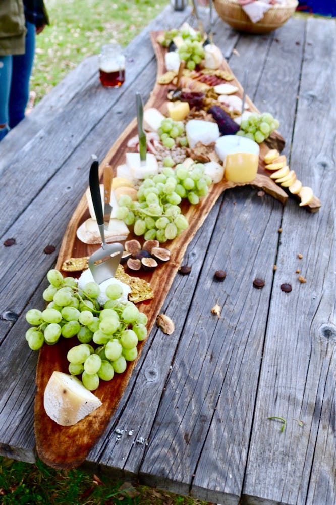 a long narrow board with cheese and fruit on it on a wooden picnic table