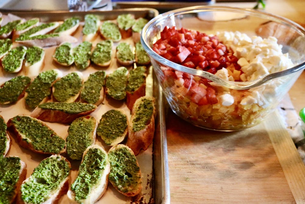 a baking dish filled with sliced bread topped with pesto next to a glass bowl of tomatoes and mozzarella