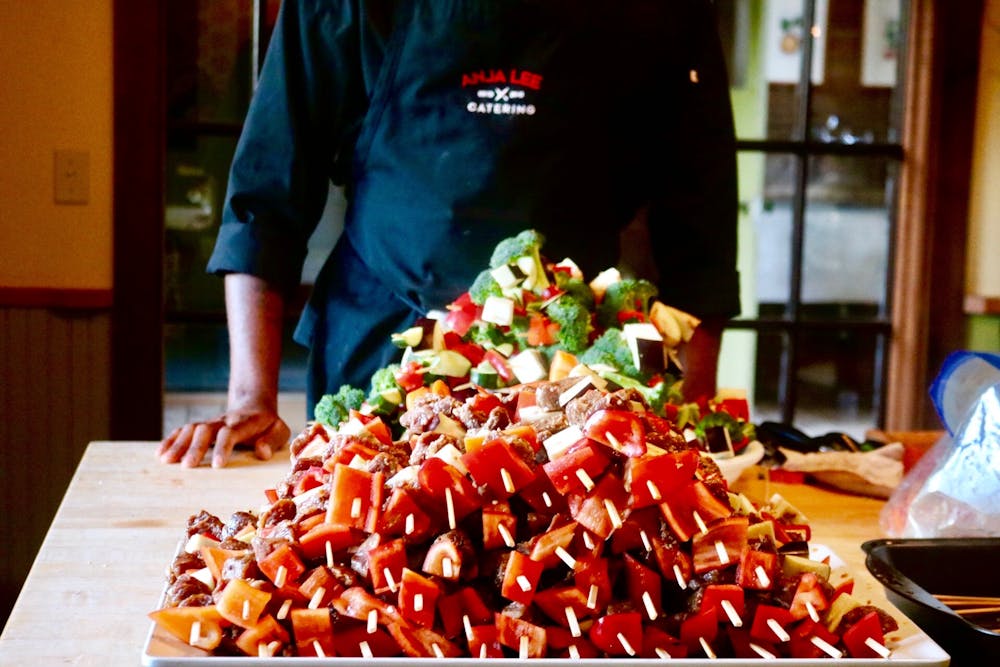 a platter of fruit kabobs and vegetables with someone in a black apron standing behind them